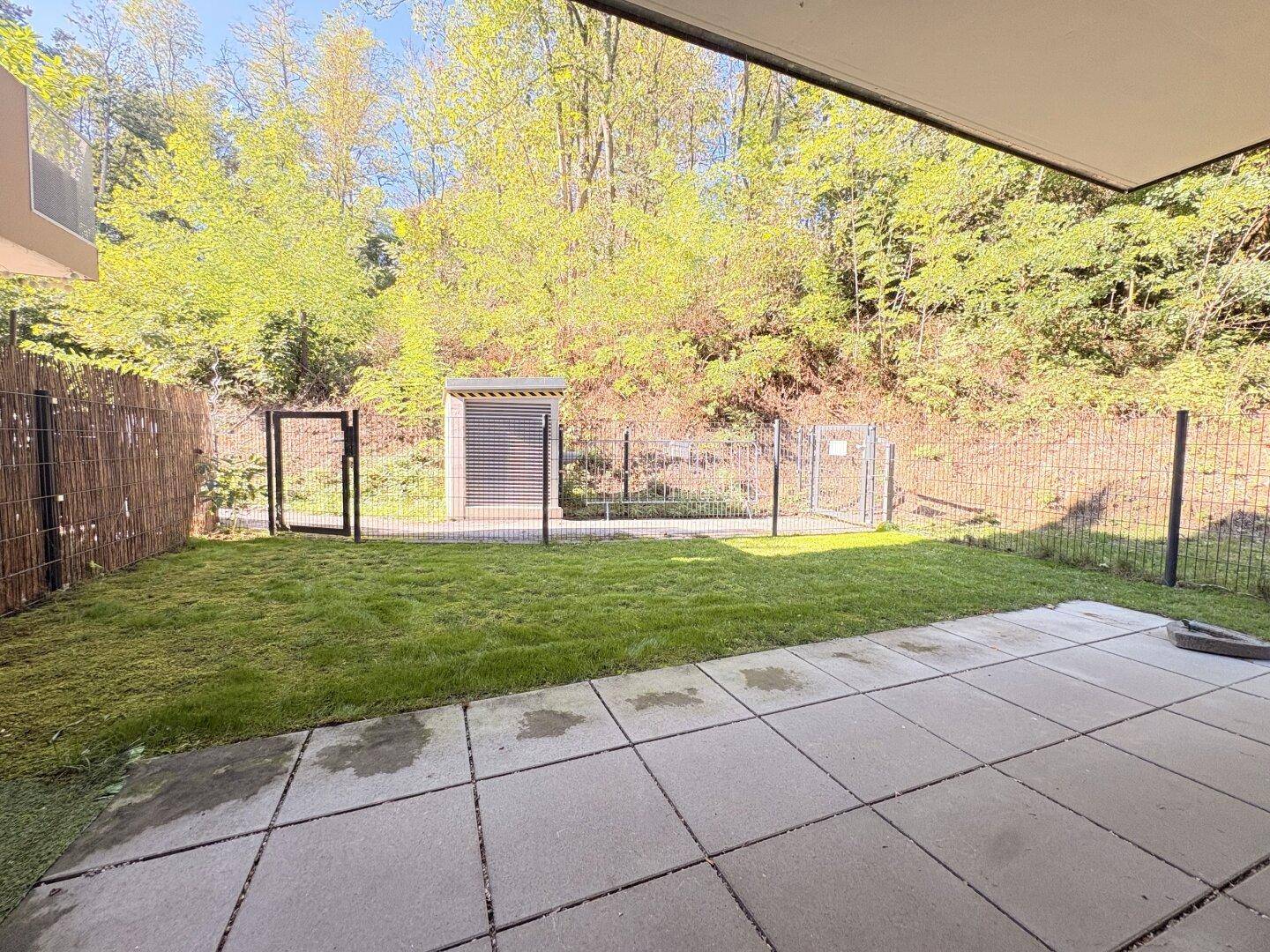 Private Terrasse mit Rasenfläche und Blick ins Grüne, umzäunt für Privatsphäre.