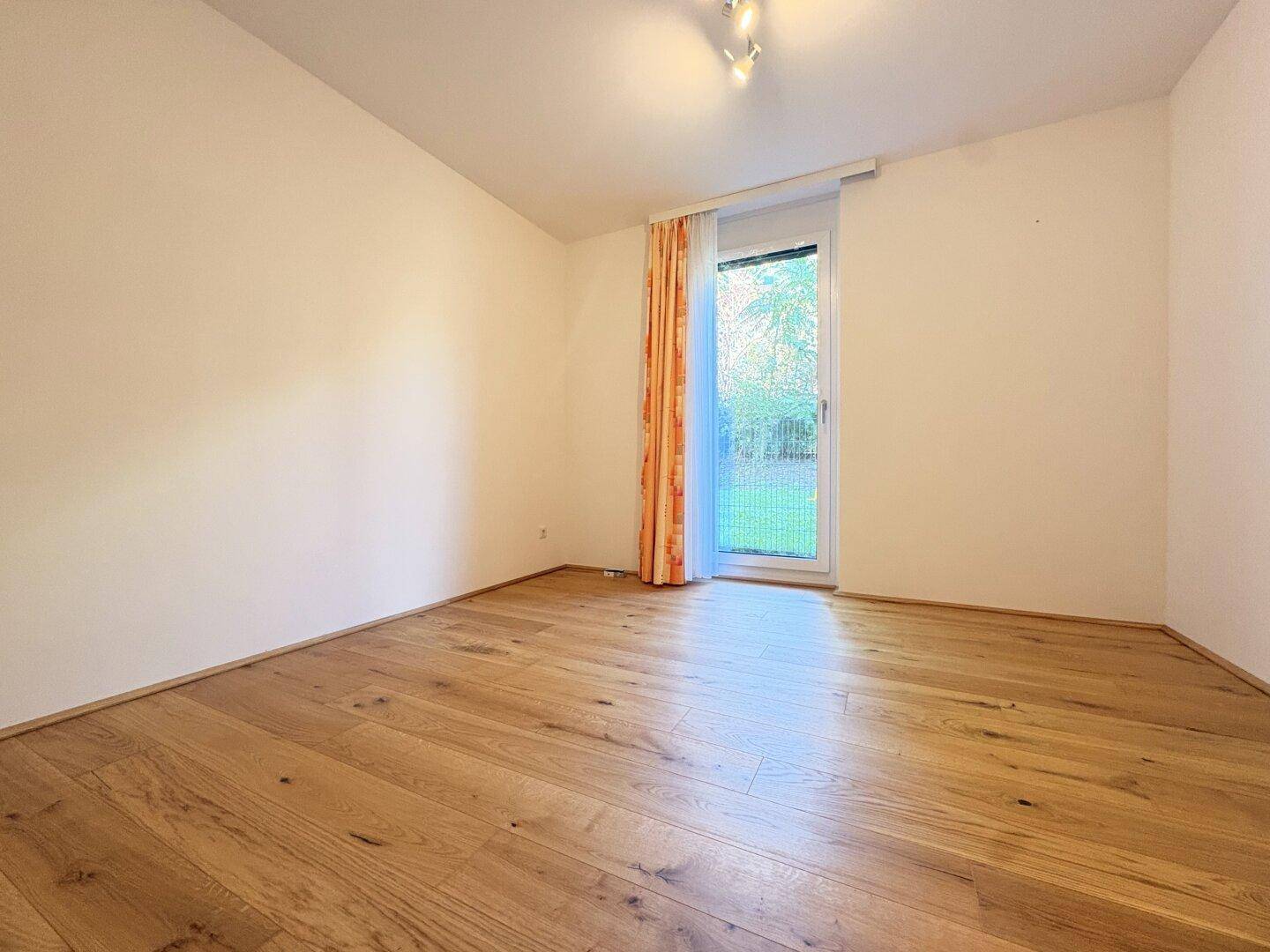 Helles Schlafzimmer mit Holzboden und Zugang zum Außenbereich durch eine Fenstertür.