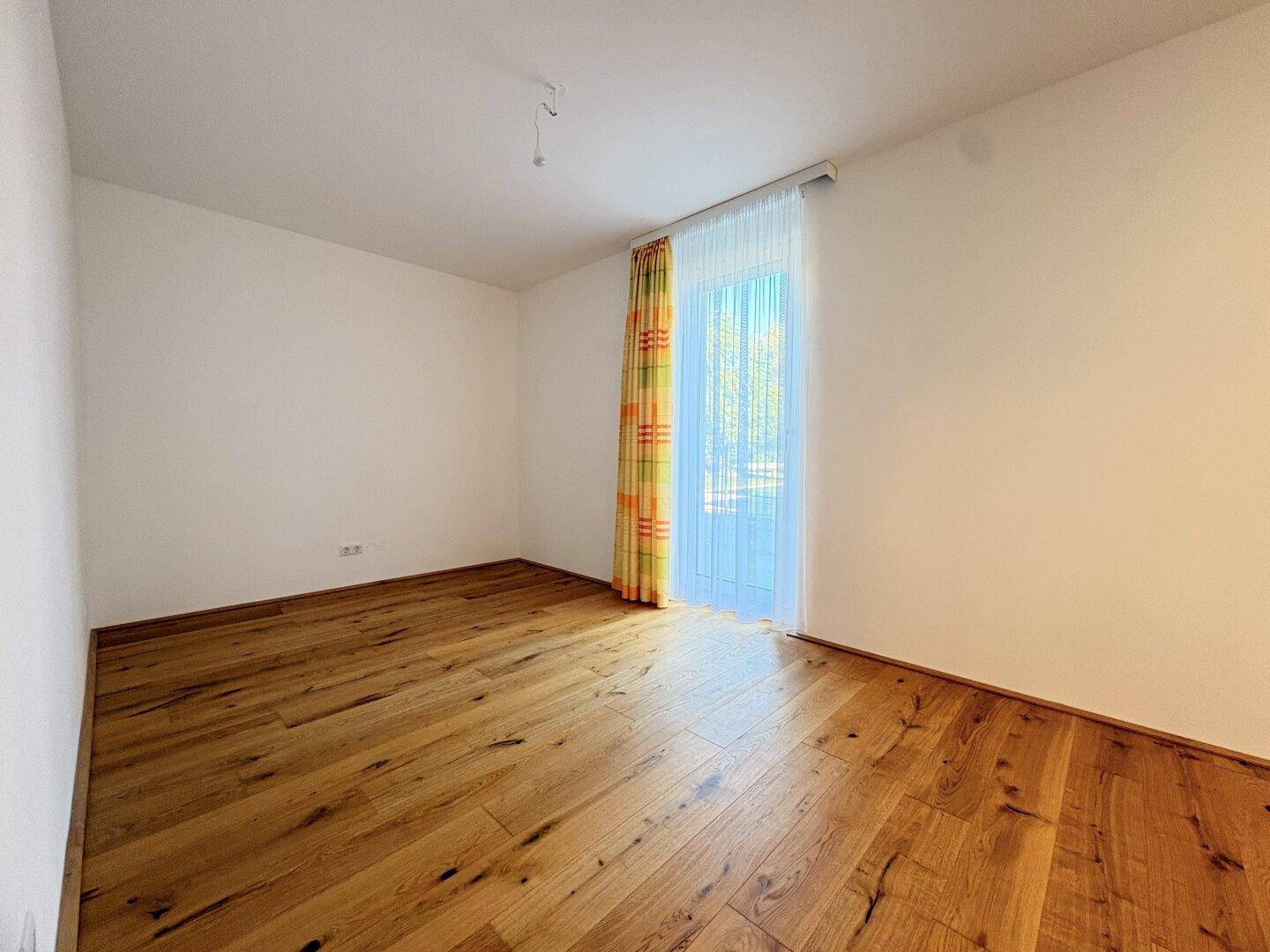Ruhiges Schlafzimmer mit Holzboden und Fenstertür, die den Raum hell erscheinen lässt.
