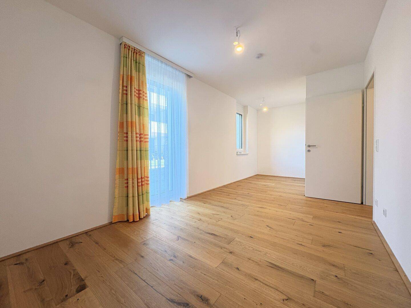 Geräumiges Schlafzimmer mit Holzboden und großen Fenstern, die viel Licht hereinlassen.