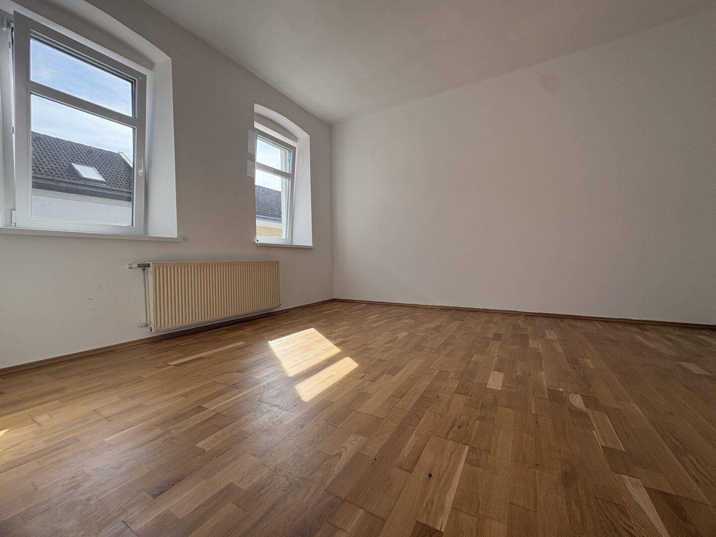 Helles Zimmer mit Holzparkettboden und zwei Fenstern, ideal als Wohn- oder Schlafzimmer.