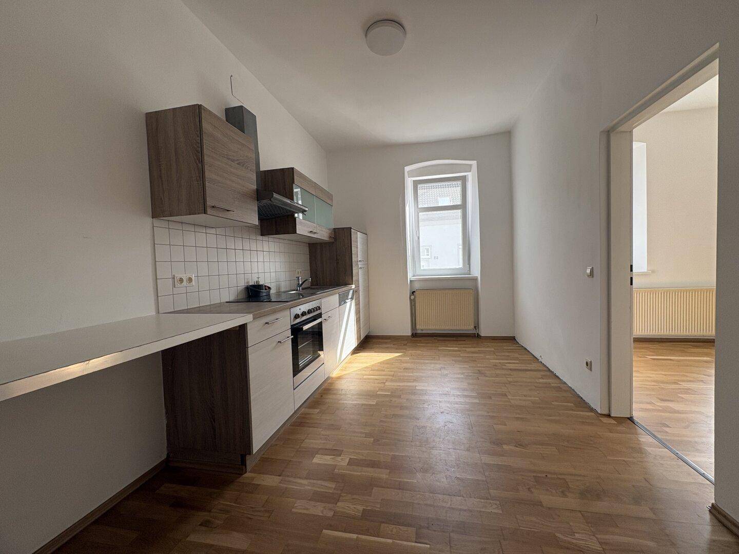 Geräumige Küche mit Einbauküche, Holzoptik-Schränken und Parkettboden, bereit zur Nutzung.