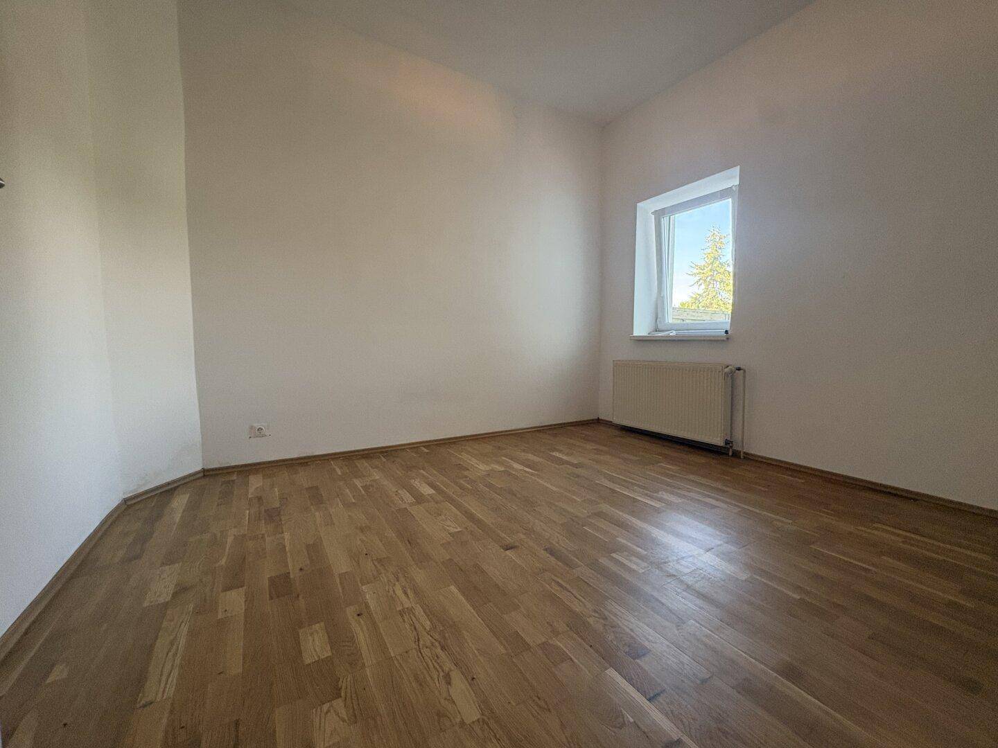 Ruhiges Schlafzimmer mit Holzparkettboden und einem Fenster, das viel Licht hereinlässt.