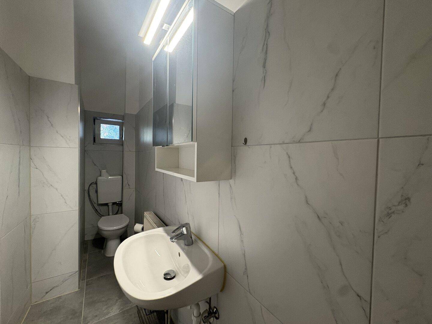 Modern gefliestes Badezimmer mit Waschbecken, Toilette und Spiegelschrank, sehr gepflegt.