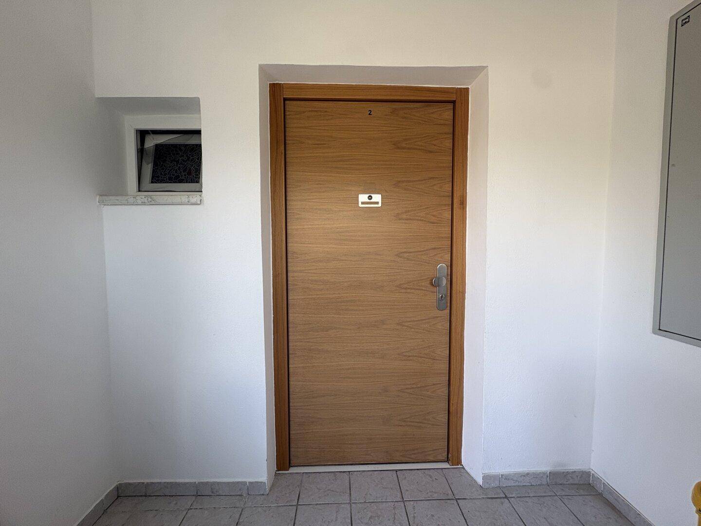 Eingangstür zu einer Wohnung in einem hellen Flur mit Fliesenboden und schlichtem Design.