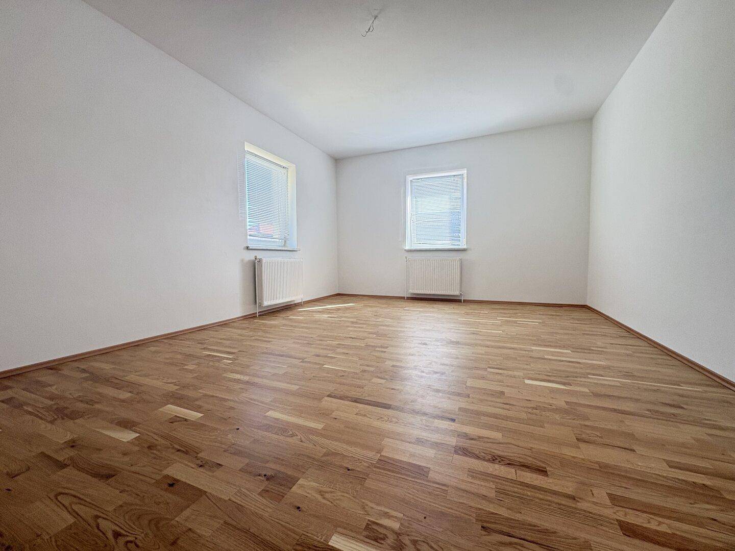 Helles Zimmer mit Holzparkettboden und zwei Fenstern, ideal als Wohn- oder Schlafzimmer.