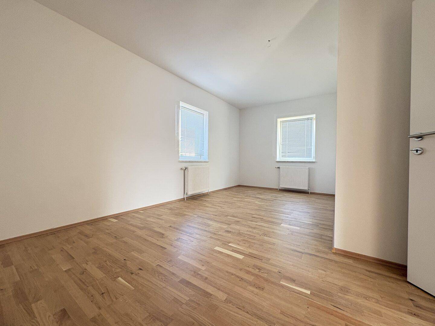 Geräumiges Zimmer mit Parkettboden und Jalousien an den Fenstern, bietet Privatsphäre.
