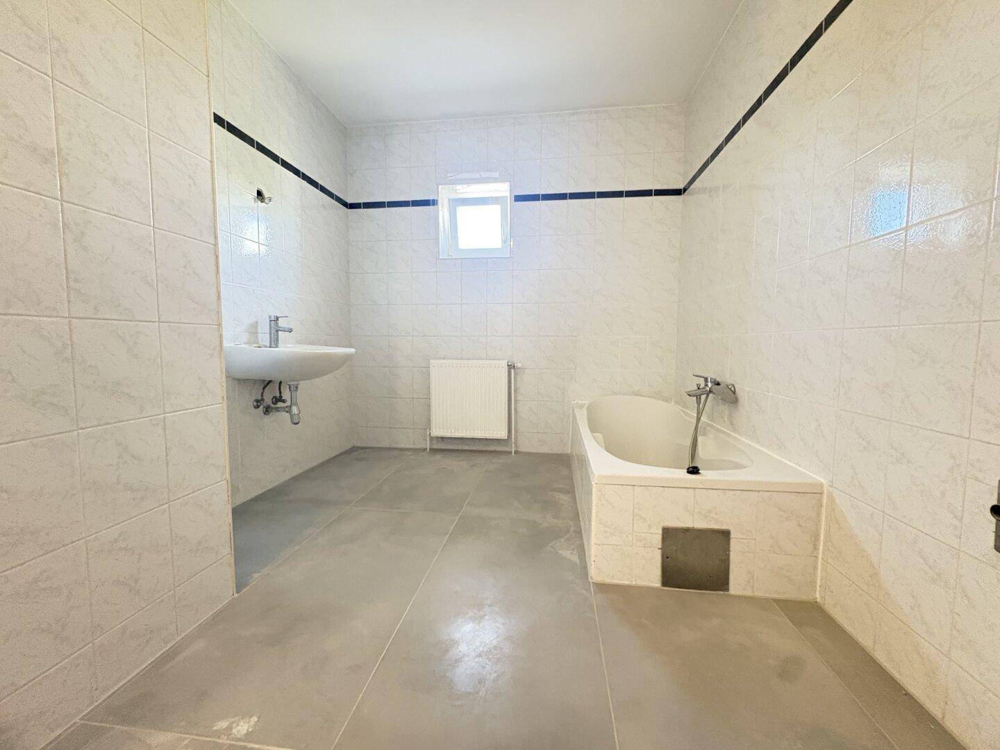 Großes Badezimmer mit Badewanne, Waschbecken und hellen Fliesen, bietet viel Platz.