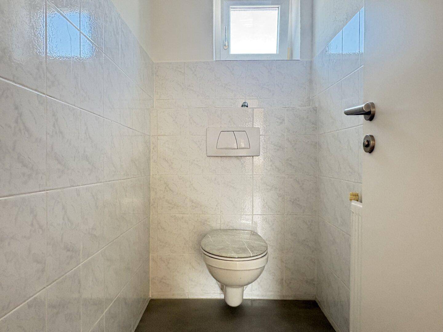 Separates WC mit wandhängender Toilette und kleinem Fenster, sehr praktisch.