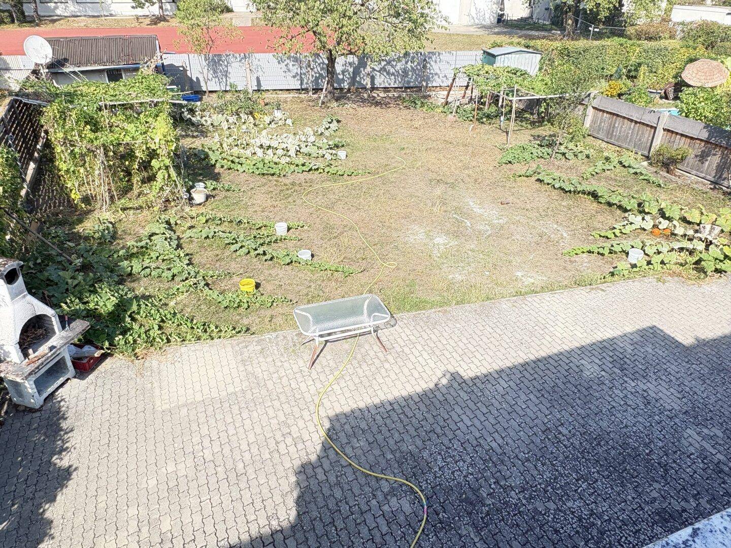 Gartenbereich mit Rasenfläche, Gemüsebeeten und gepflastertem Sitzbereich, sehr vielseitig.
