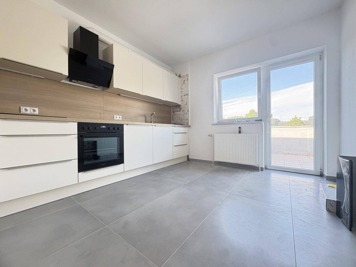 Moderne Küche mit weißen Schränken, integriertem Backofen und Zugang zur Terrasse.