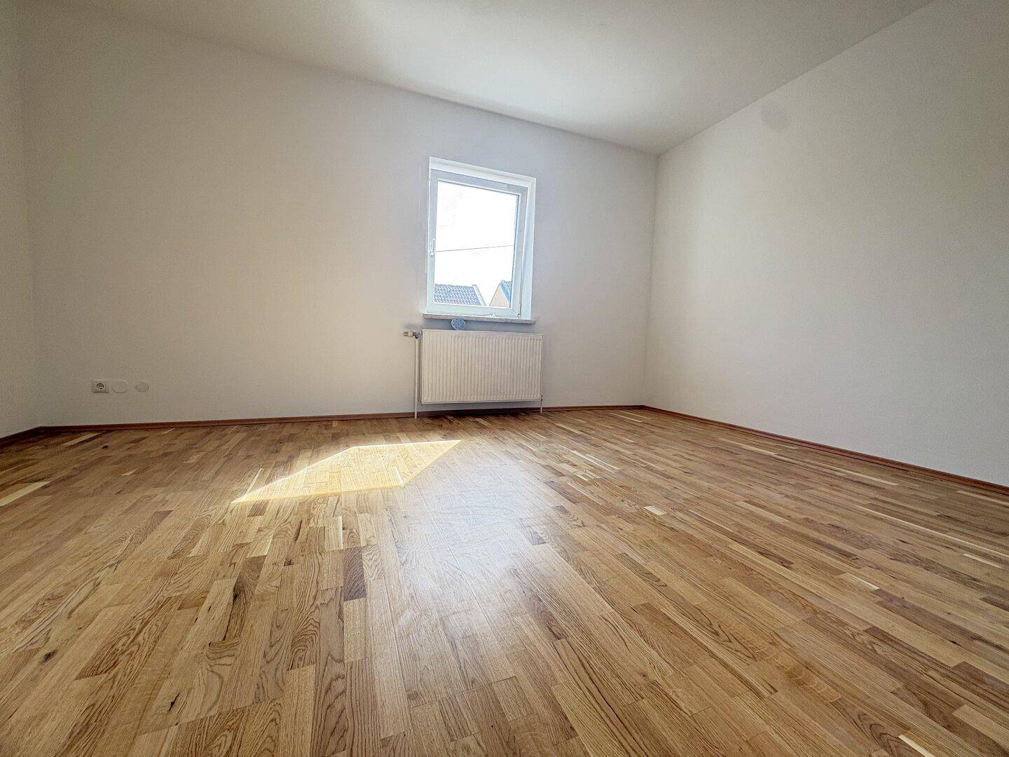 Ruhiges Schlafzimmer mit Holzparkettboden und einem Fenster, das viel Licht hereinlässt.