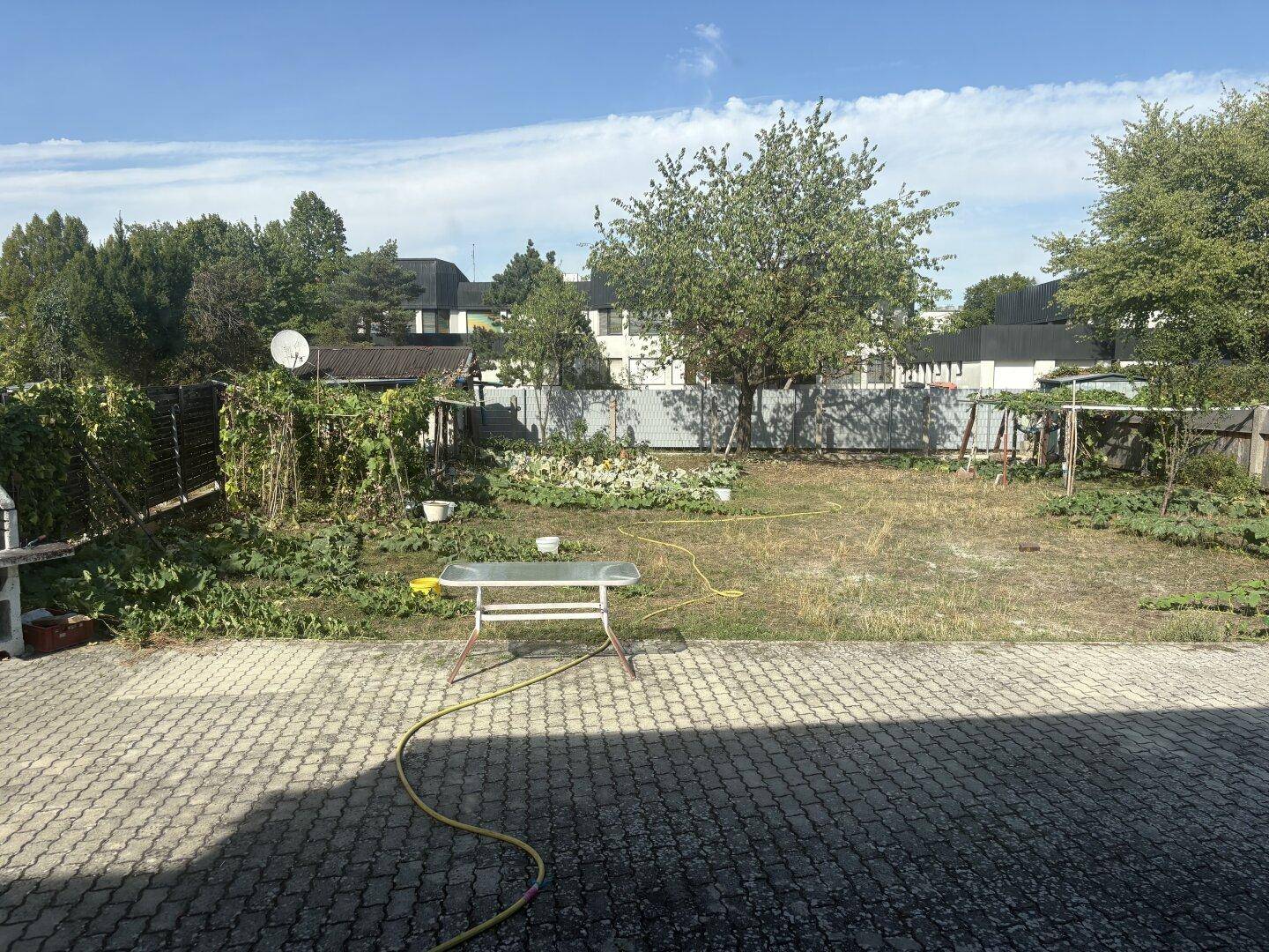 Weitläufiger Garten mit viel Grün, Bäumen und einem gepflasterten Bereich, ideal für Familien.