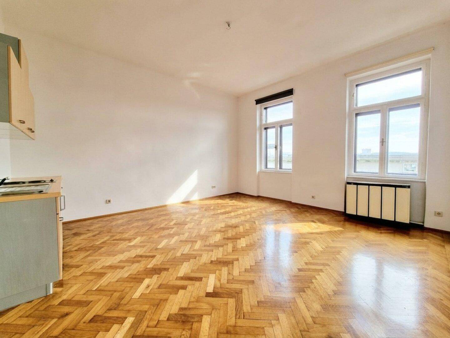 Lichtdurchfluteter Wohnbereich mit Fischgrätparkett und großen Fenstern, die viel Tageslicht hereinlassen.