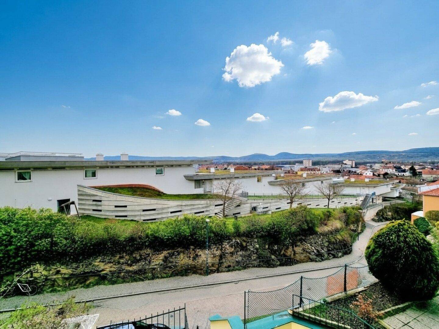 Panoramablick auf moderne Gebäude mit begrünten Dächern und die umliegende grüne Landschaft unter blauem Himmel.