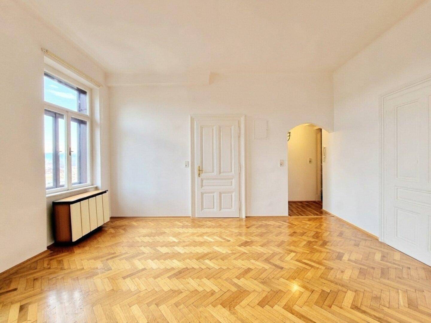 Geräumiger Wohnbereich mit klassischem Fischgrätparkett und hohen Türen, der vielseitige Gestaltungsmöglichkeiten bietet.