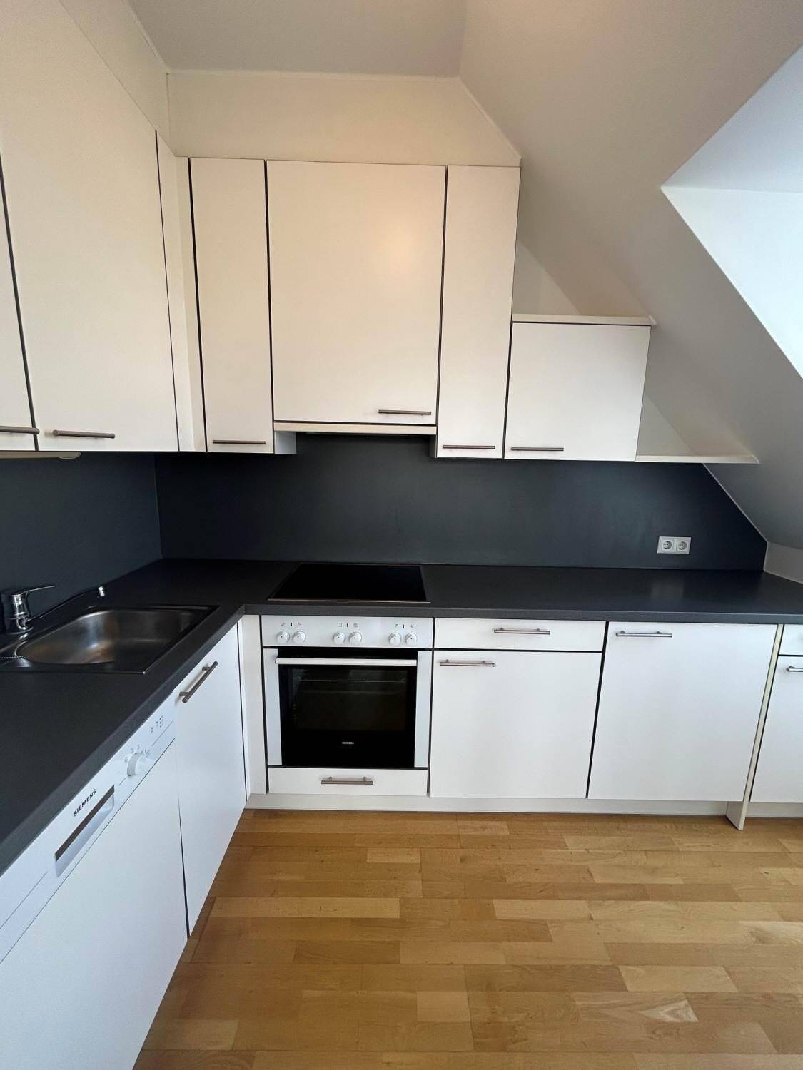 Moderne Einbauküche mit weißen Schränken, dunkler Arbeitsplatte und integrierten Geräten.