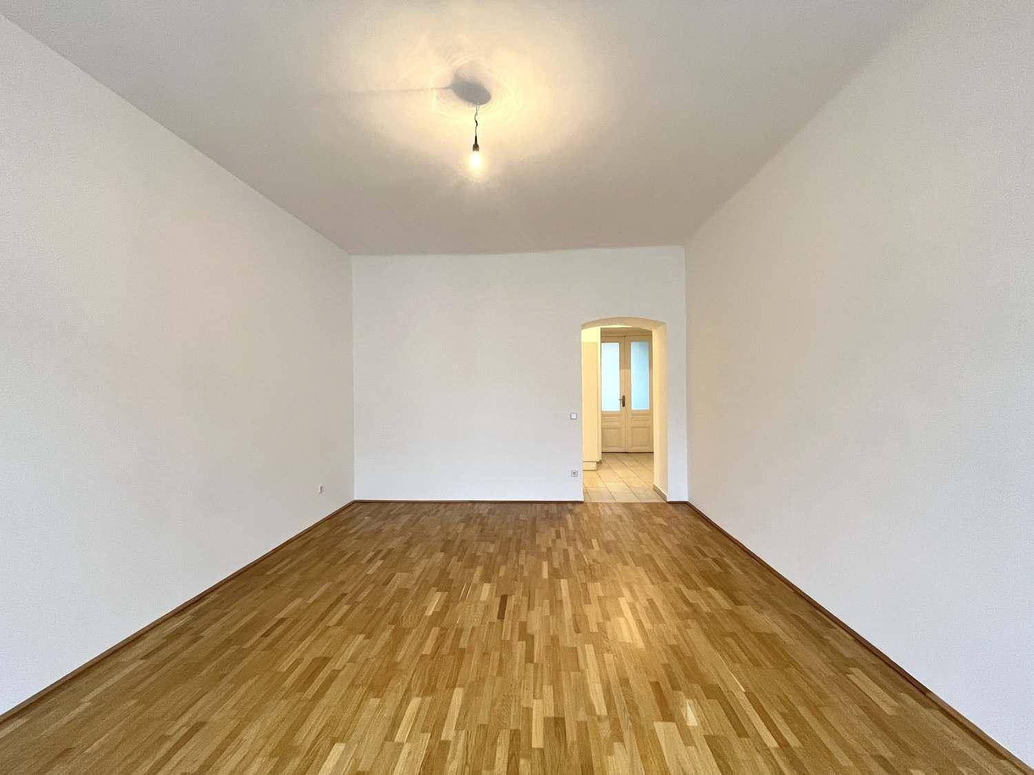 Leeres Wohnzimmer mit Parkettboden und einem Durchgang zu einem weiteren Raum.