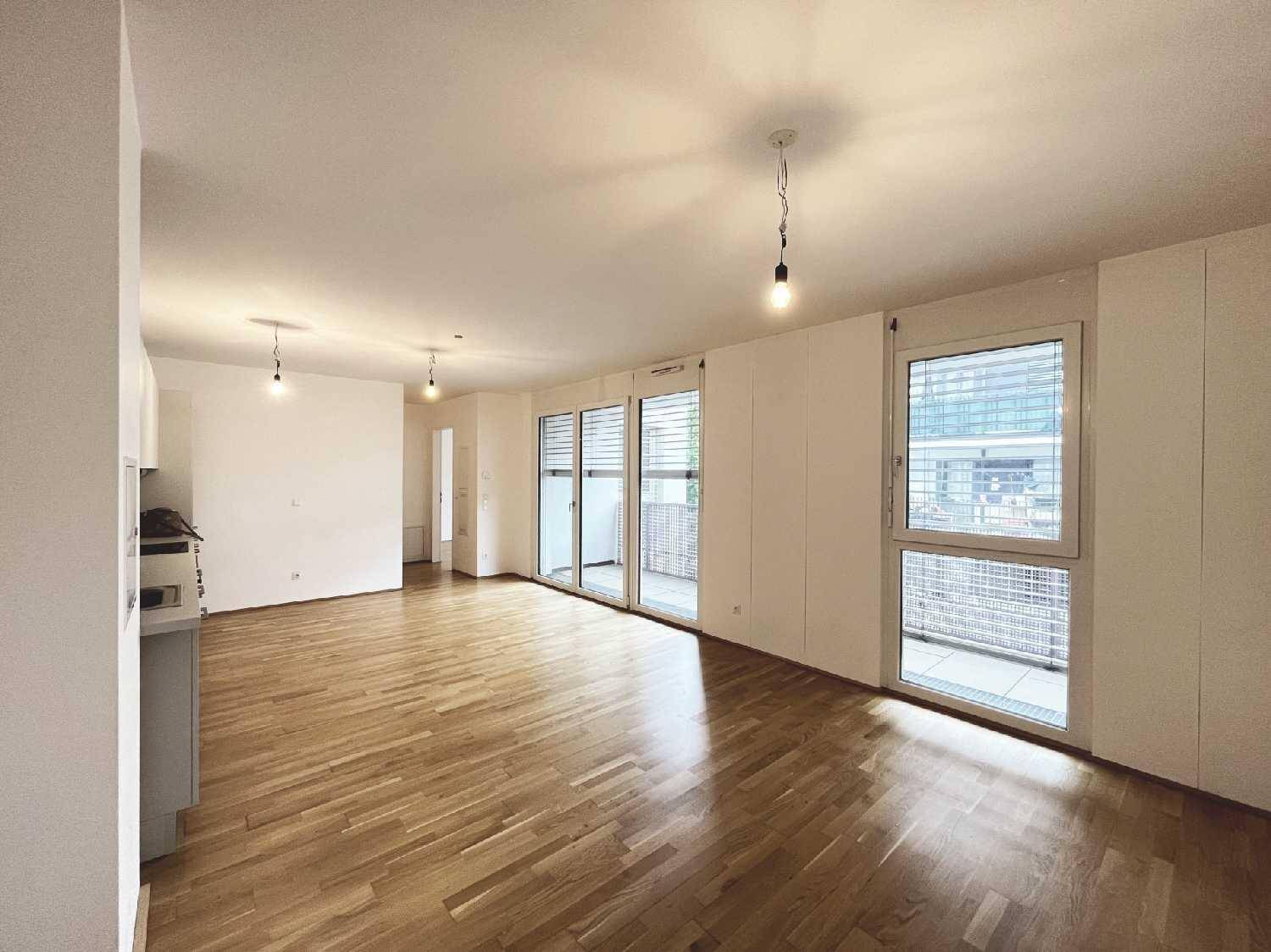 Geräumiger Wohnbereich mit hellem Parkettboden und Zugang zu einem Balkon durch große Fensterfronten.