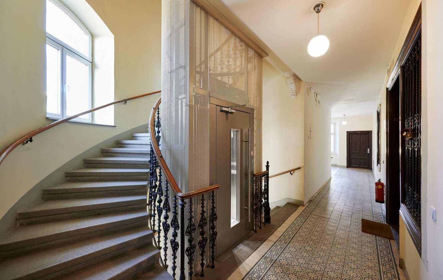 Historisches Treppenhaus mit elegantem Geländer und einem modernen Aufzug für bequemen Zugang.