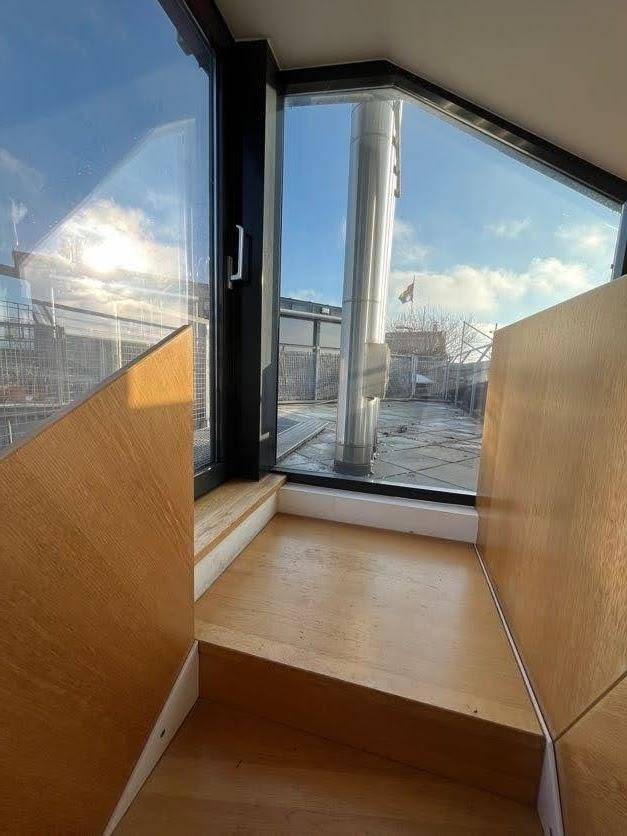 Kleiner Treppenabsatz mit Holzverkleidung und Blick durch ein großes Fenster nach draußen.