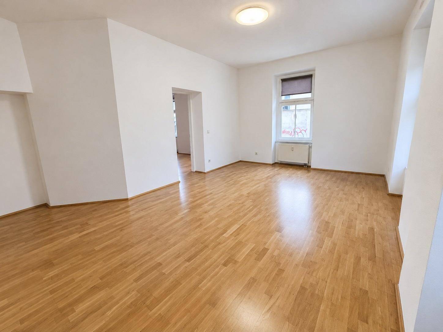Geräumiges Wohnzimmer mit hellem Parkettboden und einem Fenster, das den Raum gut belichtet.
