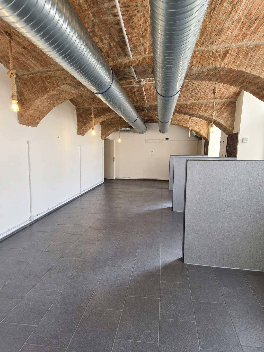 Langer, offener Raum mit Gewölbedecke, sichtbaren Lüftungsrohren und dunklem Fliesenboden.