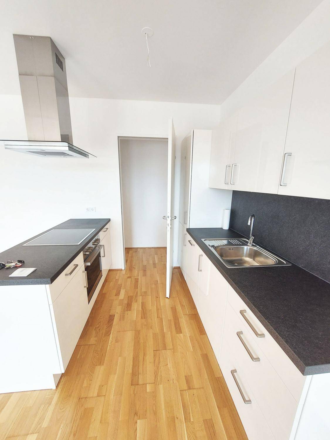 Moderne Einbauküche mit weißen Schränken, dunkler Arbeitsplatte und Kochinsel.