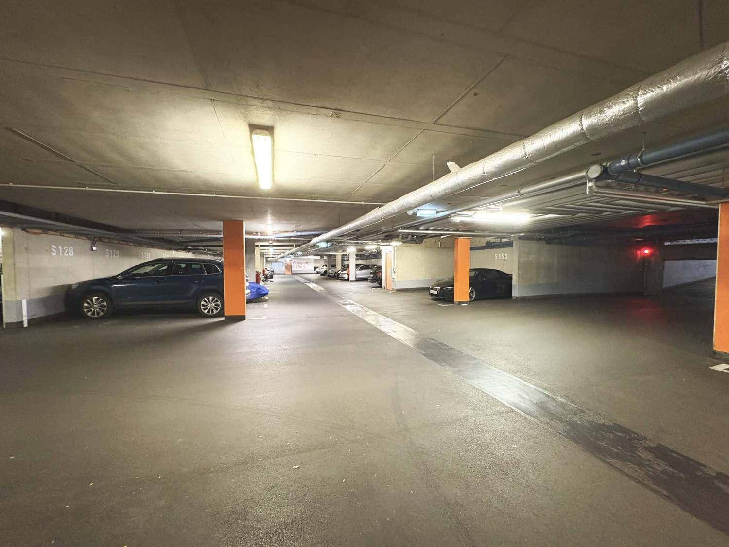 Helle Tiefgarage mit markierten Stellplätzen und orangefarbenen Säulen.