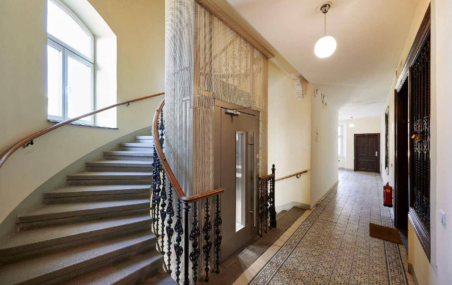 Historisches Treppenhaus mit geschwungener Treppe, Aufzug und gemusterten Fliesen im Eingangsbereich.