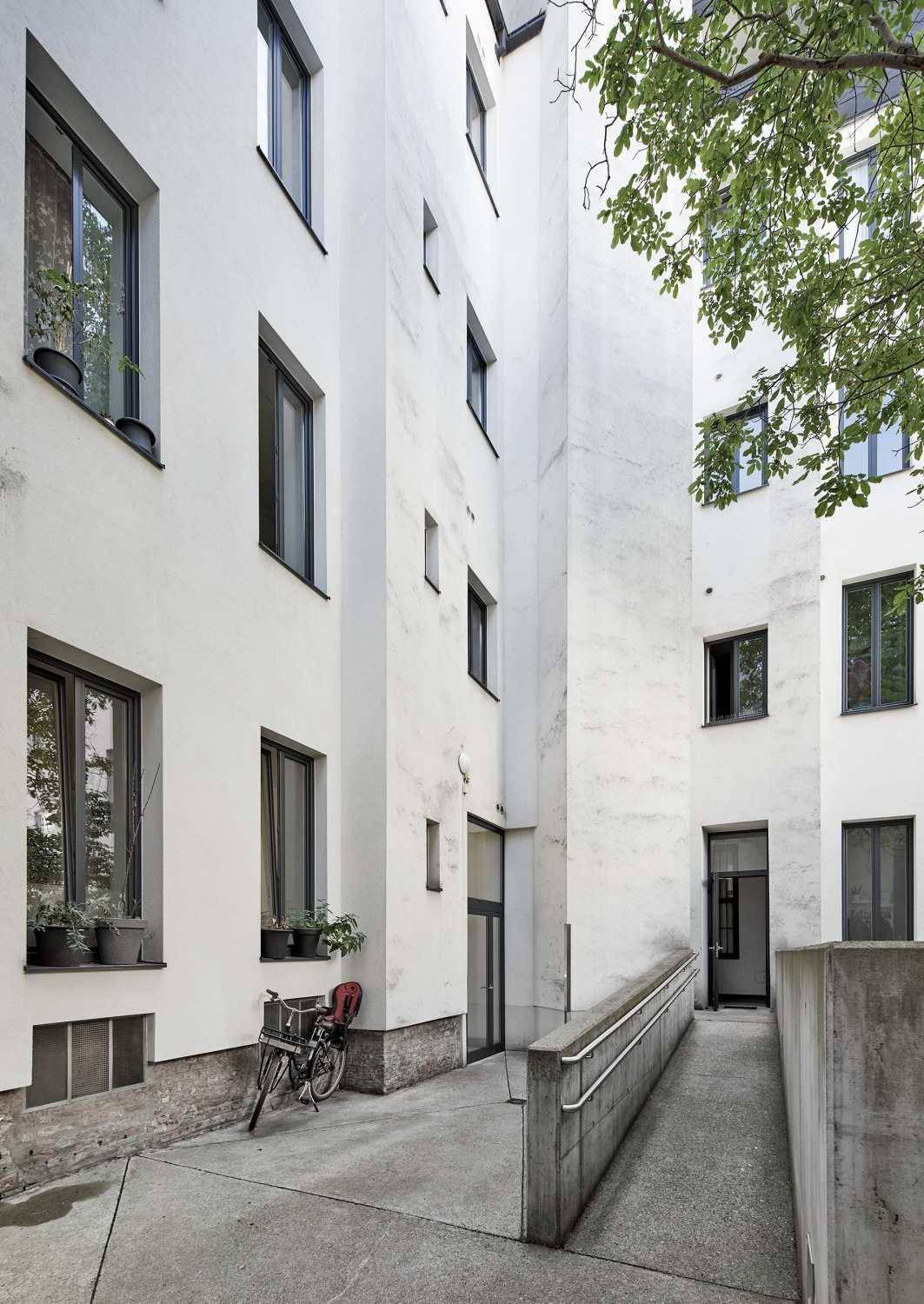 Hinterhof mit Rampe und Zugang zu den Wohnungen, umgeben von weißen Fassaden.