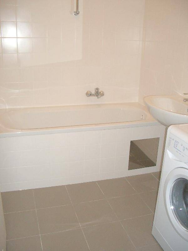 Badezimmer mit Badewanne, Waschbecken und Waschmaschine, gefliest in hellen Tönen.