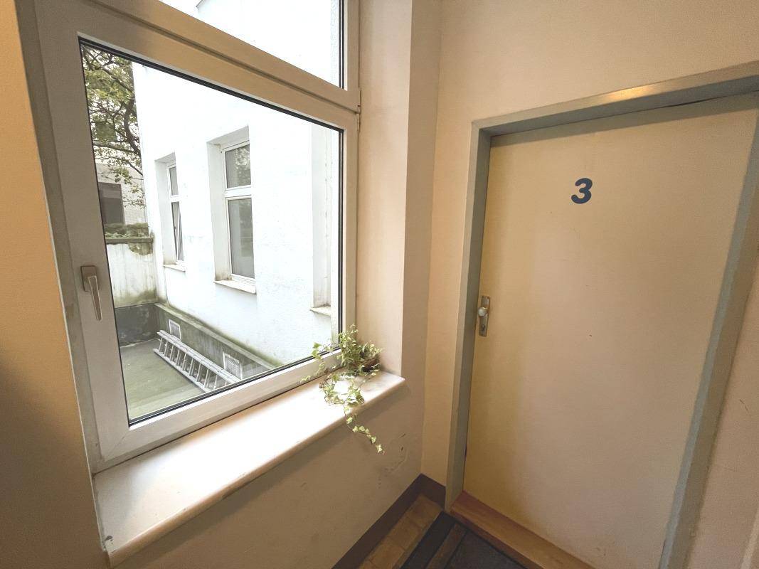 Heller Treppenabsatz mit Fenster und Blick auf einen kleinen Innenhof.