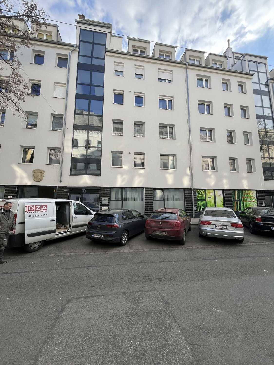 Mehrstöckiges Wohngebäude mit moderner Architektur, Glasfassade und geparkten Fahrzeugen davor.