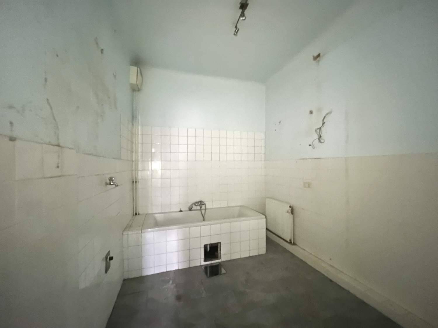 Badezimmer mit Badewanne und weißen Fliesen, das auf eine Renovierung wartet.