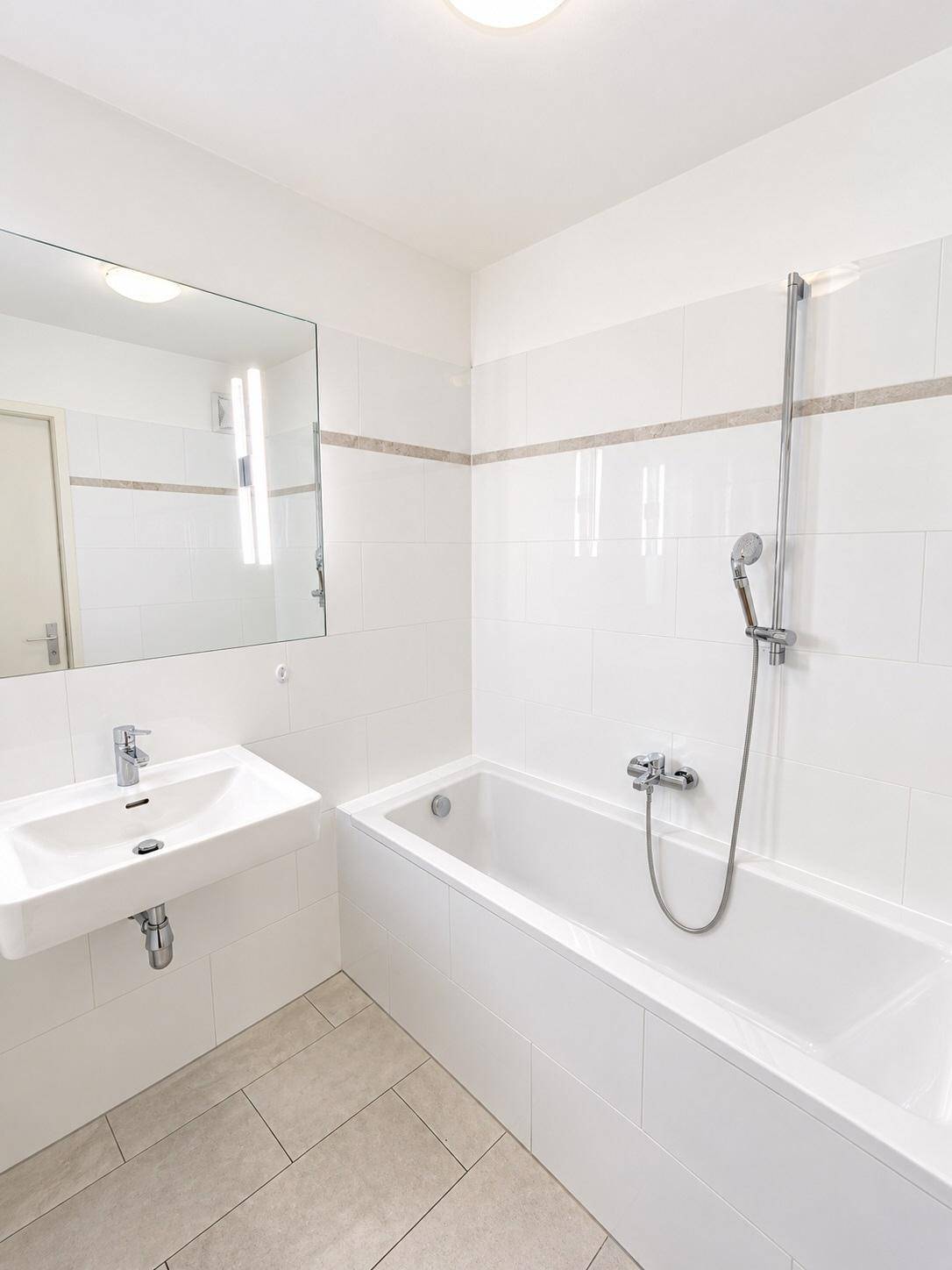 Modernes Badezimmer mit Badewanne, Waschbecken und weißen Fliesen an Wänden und Boden.