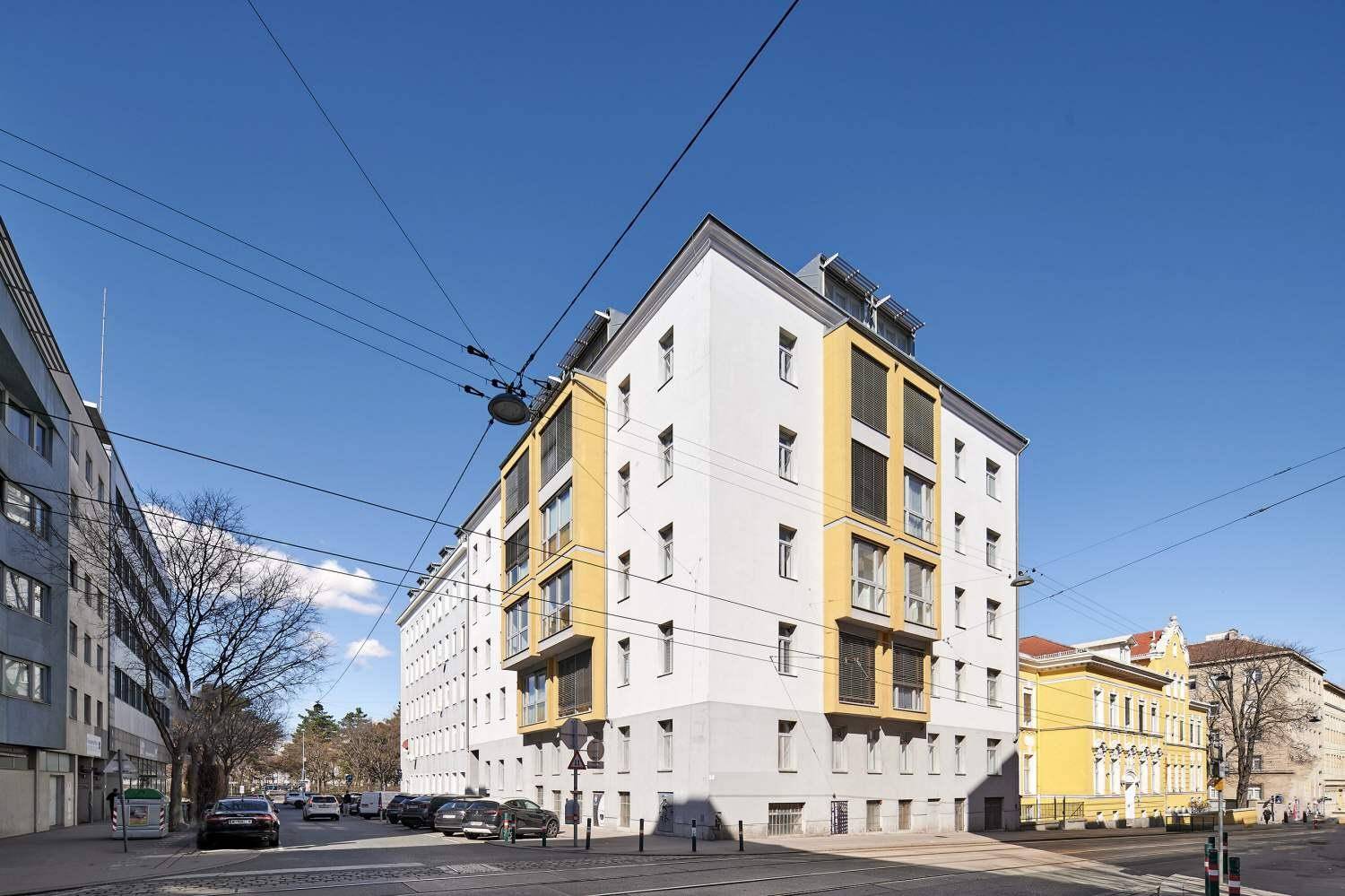 Weitwinkelansicht des modernen Gebäudes mit gelben Fassadenelementen an einer städtischen Straße.