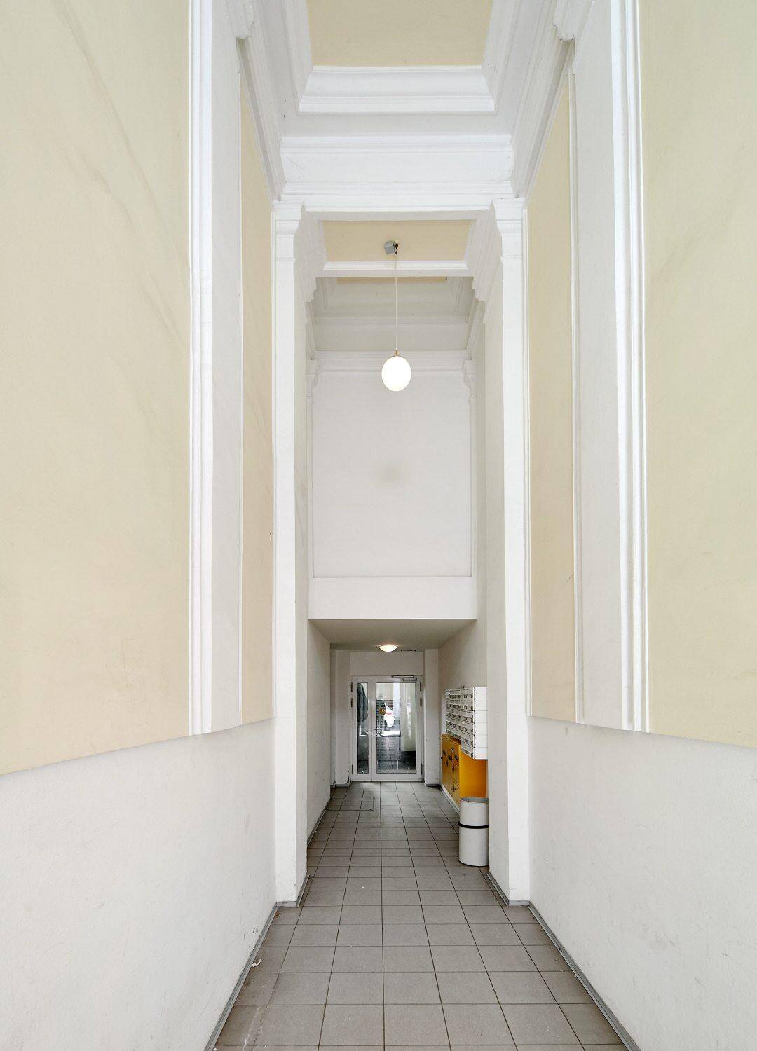 Langer, heller Eingangsbereich eines Altbaus mit hohen Decken und Fliesenboden.