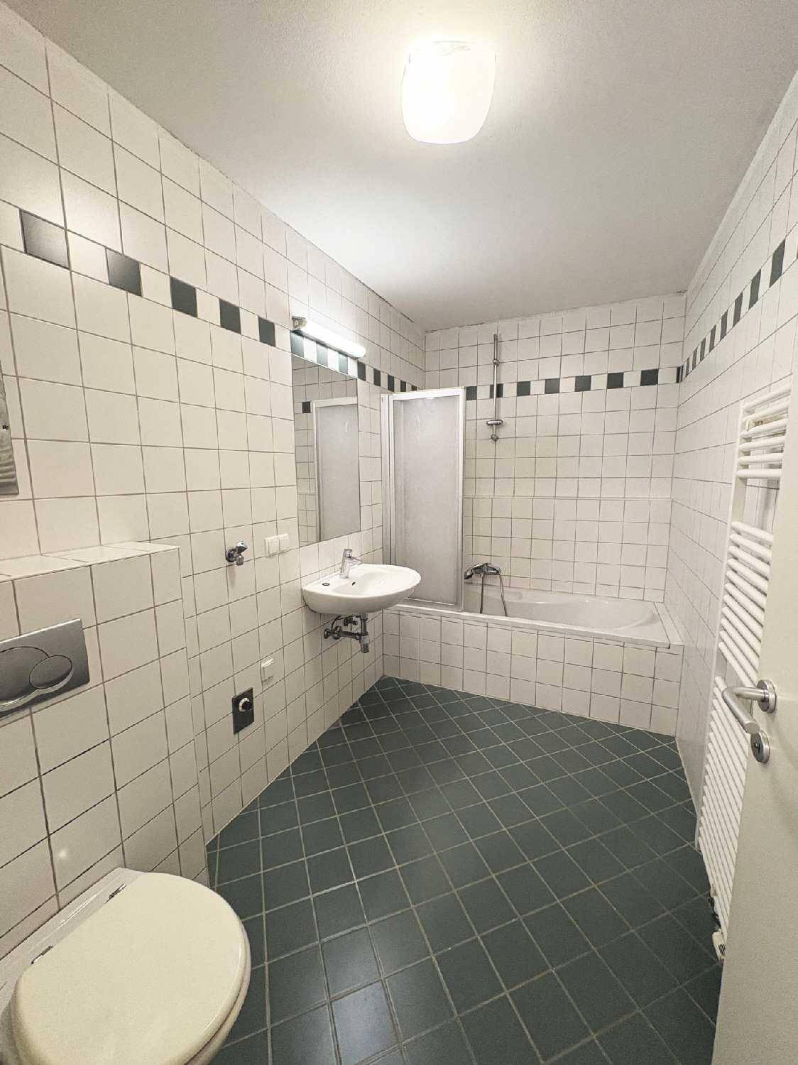 Badezimmer mit weißen Wandfliesen, dunkelgrauem Fliesenboden, Badewanne mit Duschfunktion und beheiztem Handtuchhalter.