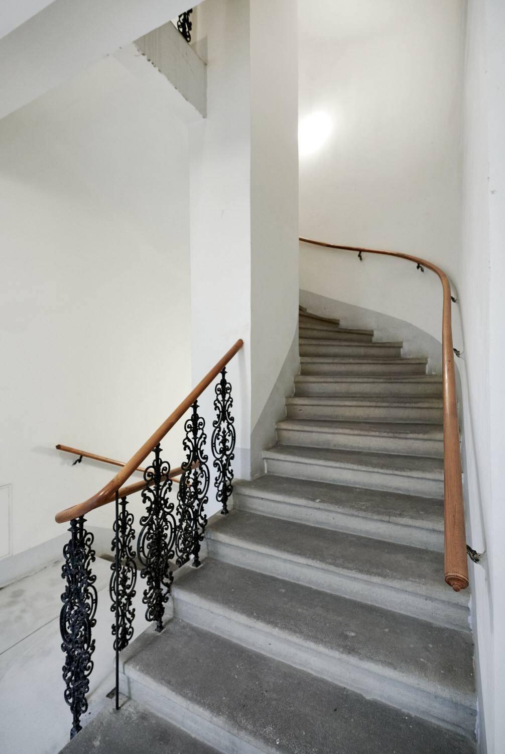 Historisches Treppenhaus mit schmiedeeisernem Geländer und Holzhandlauf in einem Altbau.