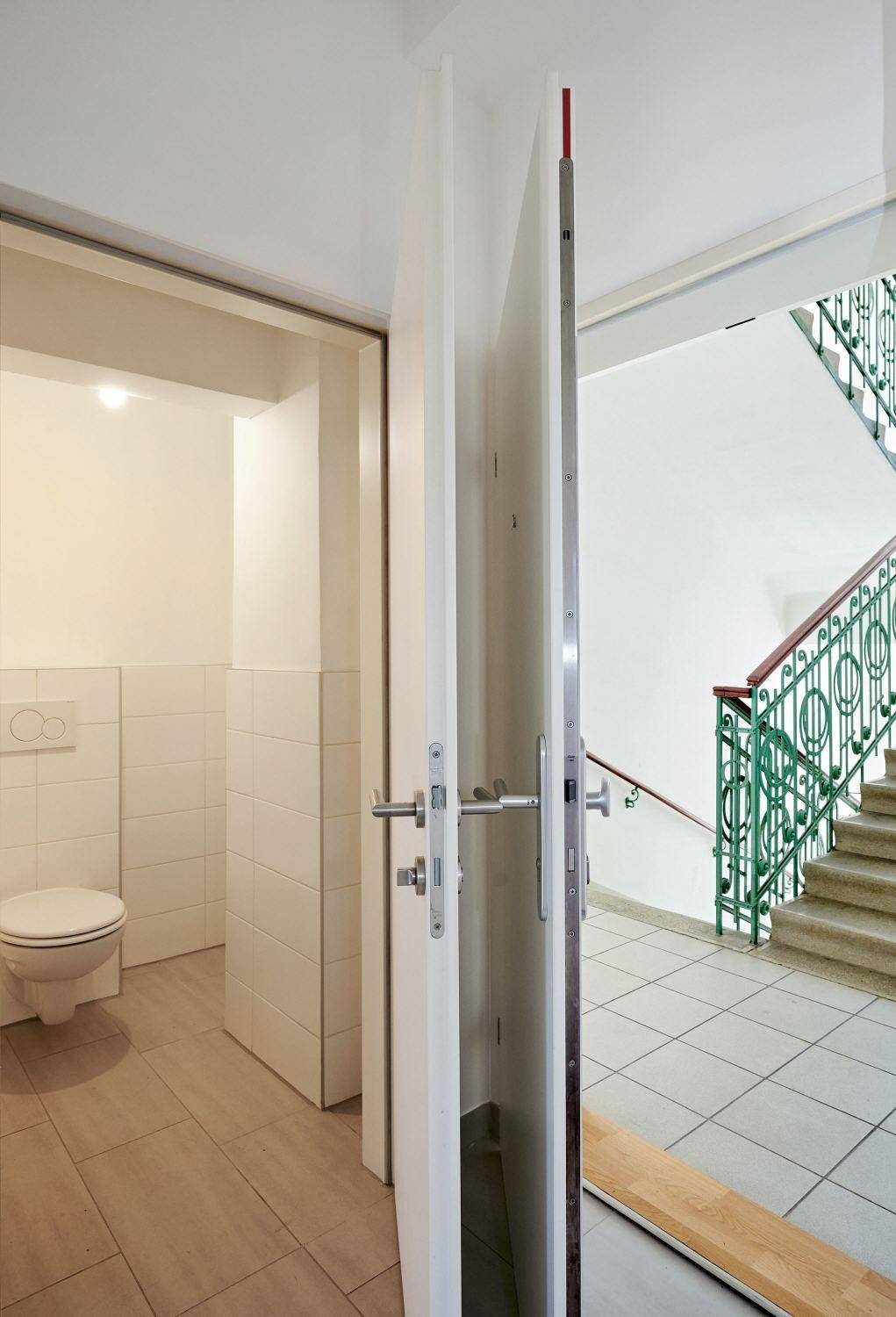 Eingangsbereich mit Zugang zur Gästetoilette und Blick auf das Treppenhaus mit grünem Geländer.