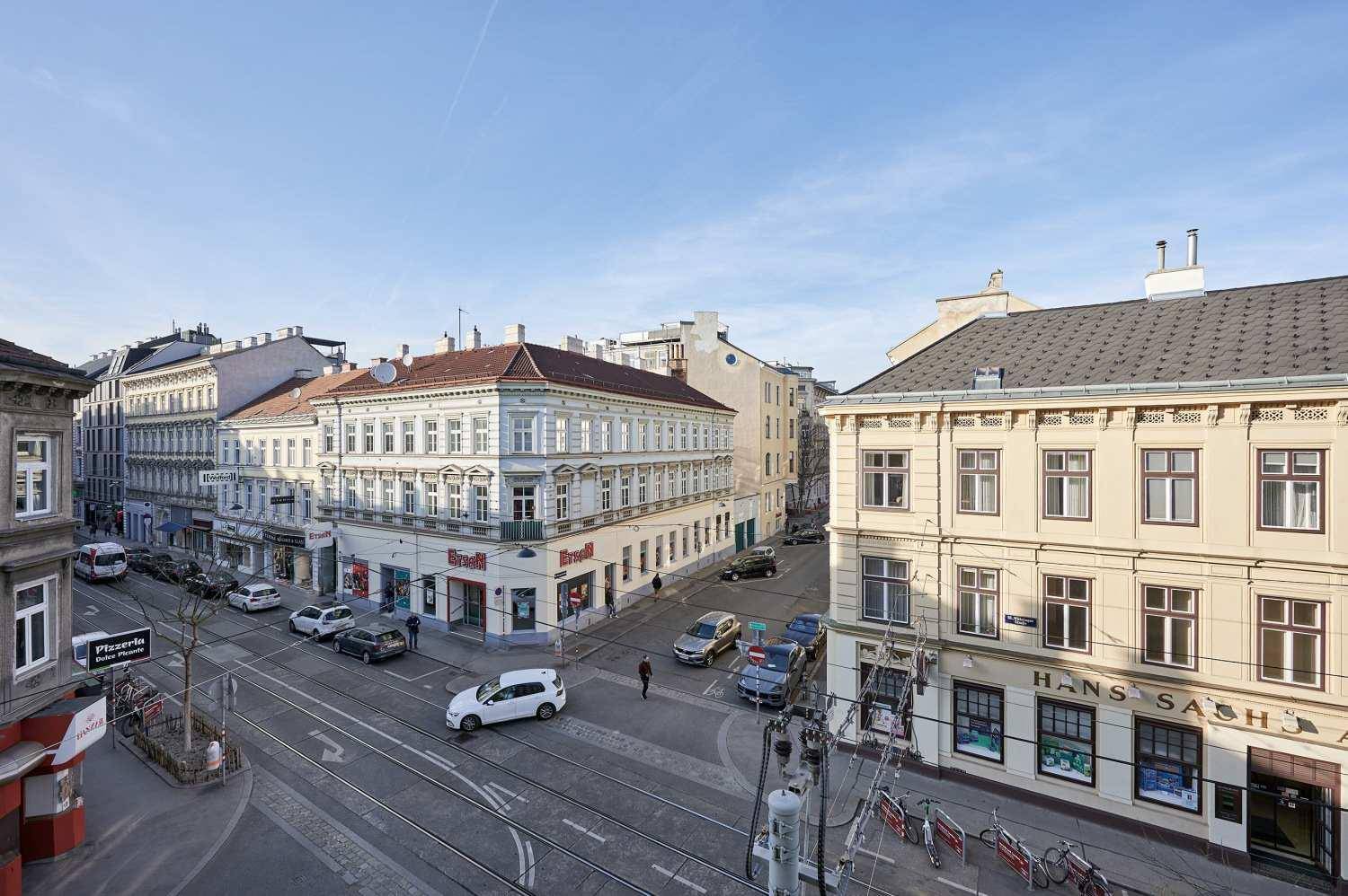Erhöhte Ansicht einer belebten Stadtstraße mit historischen Gebäuden, Fahrzeugen und Straßenbahnschienen.