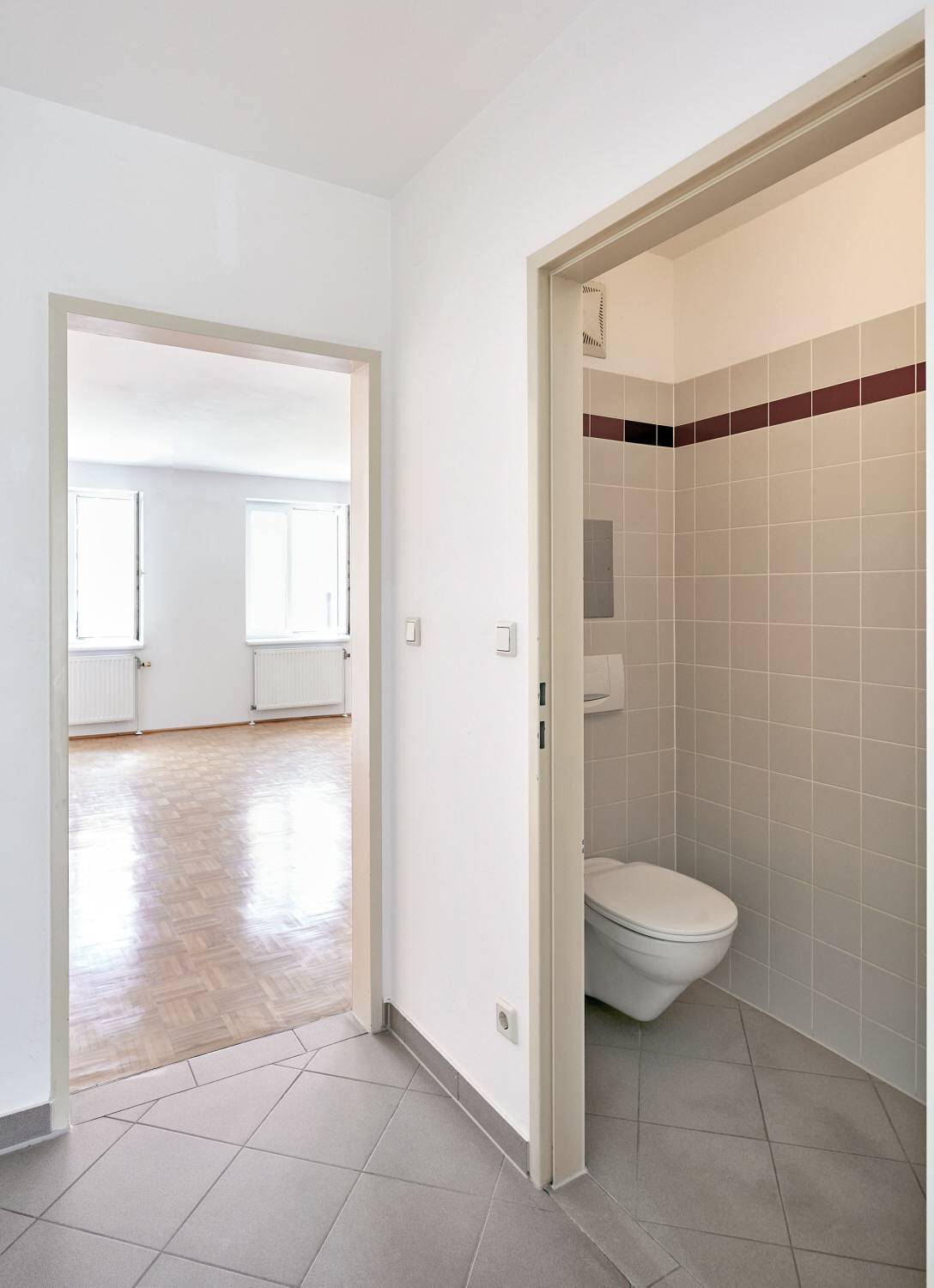 Flur mit Fliesenboden, Zugang zu einem separaten WC und Blick in den Wohnbereich.