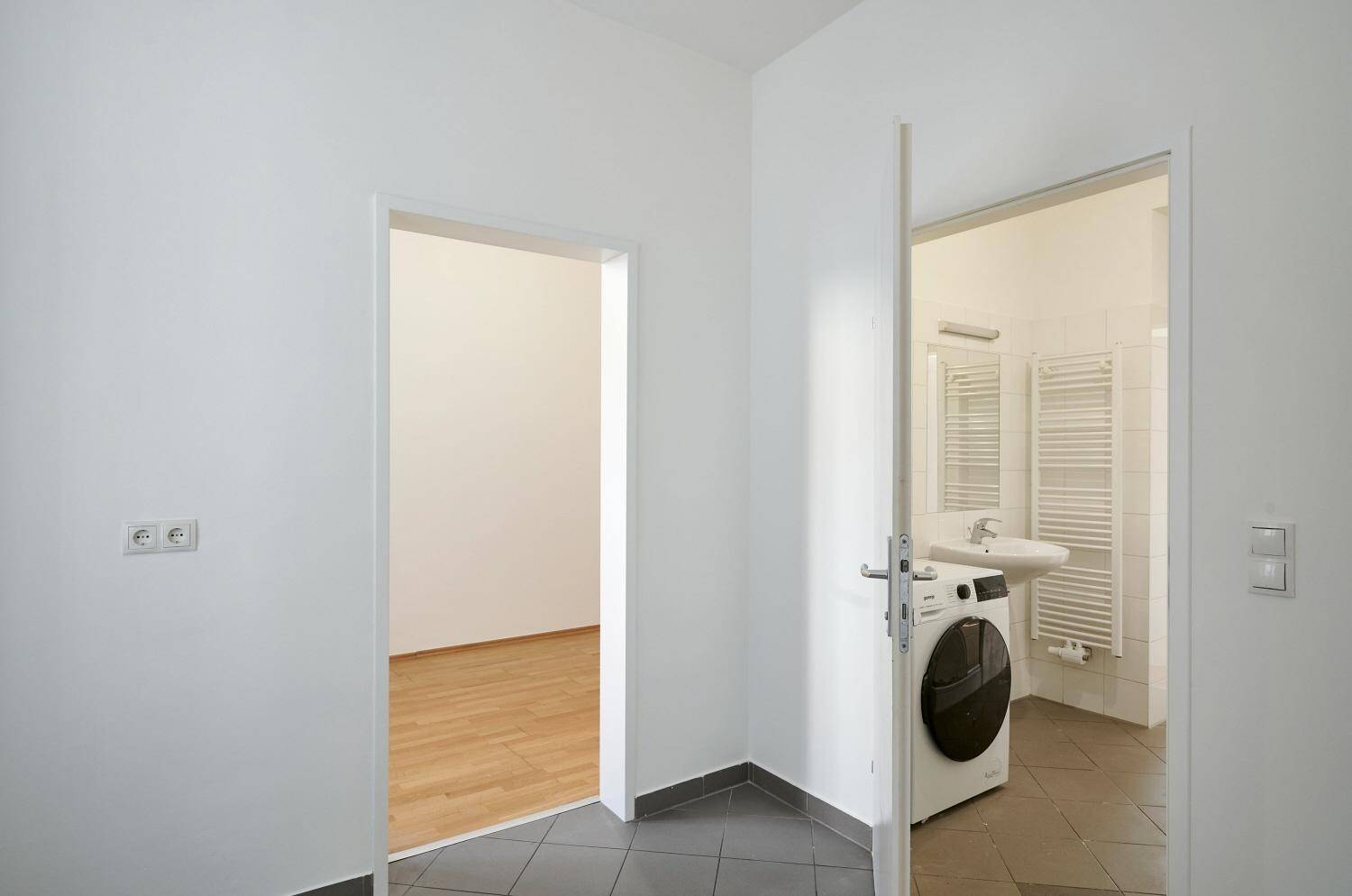 Heller Flur mit Zugang zu einem Badezimmer und einem weiteren Zimmer mit Parkettboden.