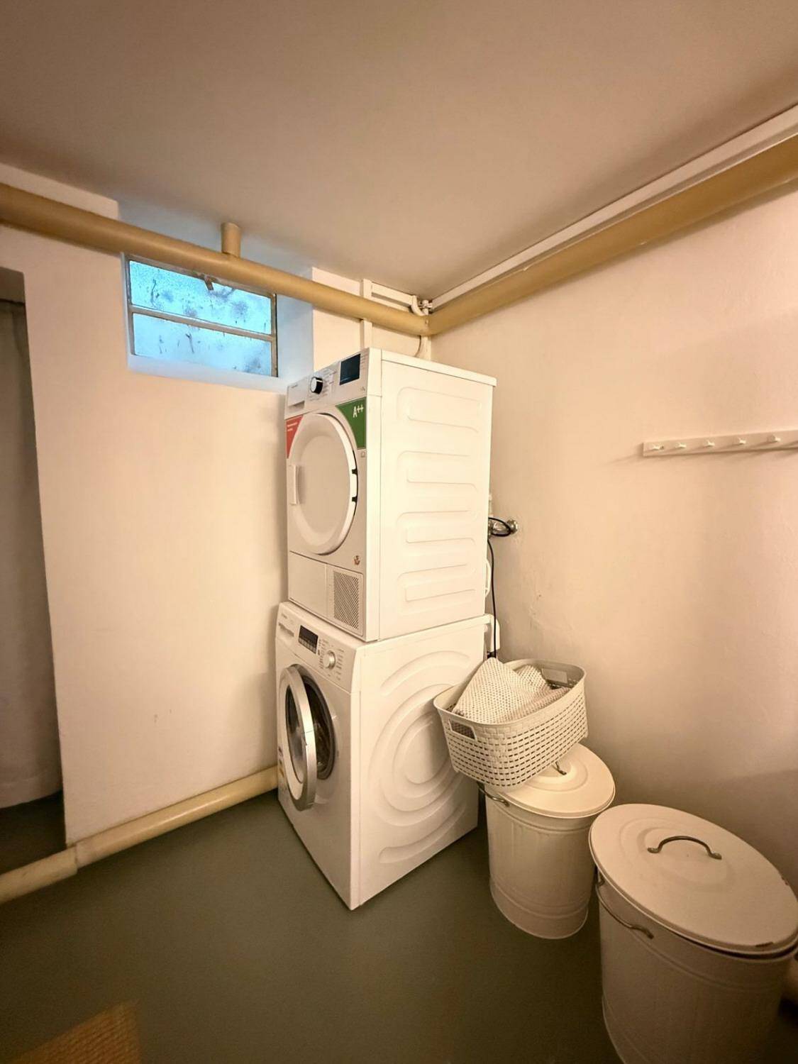 Waschküche im Keller mit Waschmaschine, Trockner und kleinem Fenster.