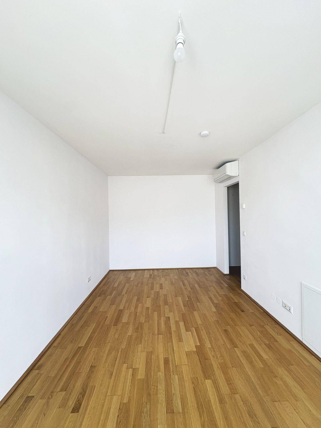 Leerer Raum mit Holzboden, weißen Wänden und Klimaanlage, bereit zur individuellen Gestaltung.