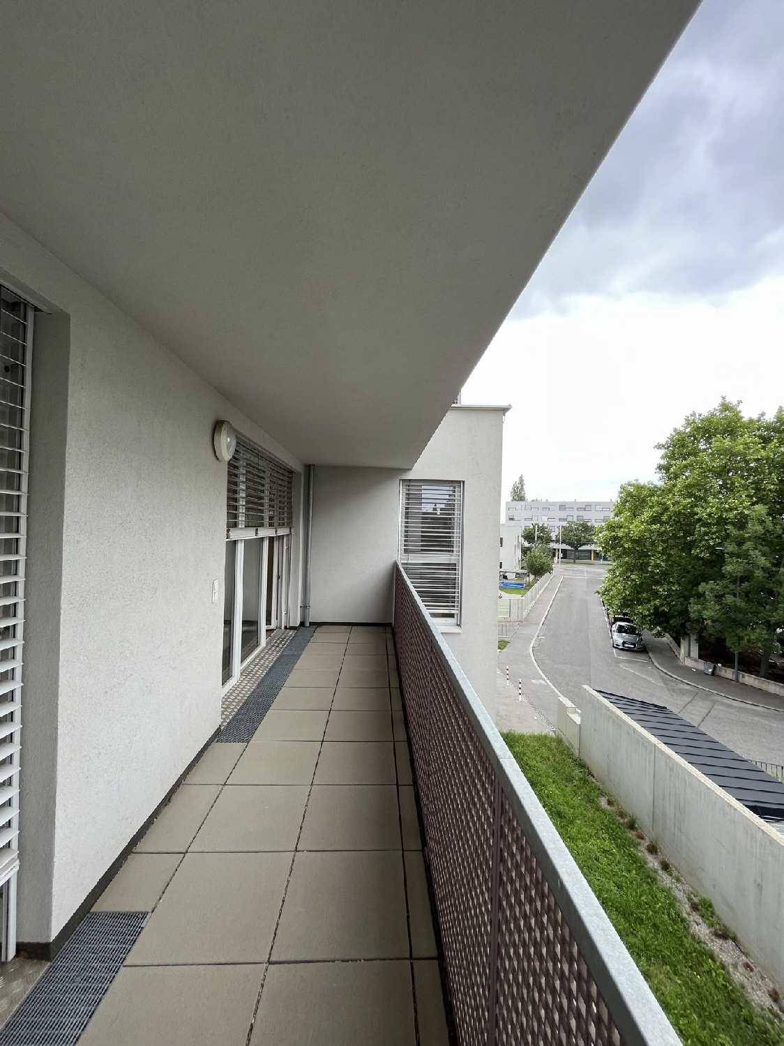 Langer Balkon mit Fliesenboden und Blick auf die ruhige Straße und die umliegende Wohngegend mit Bäumen.