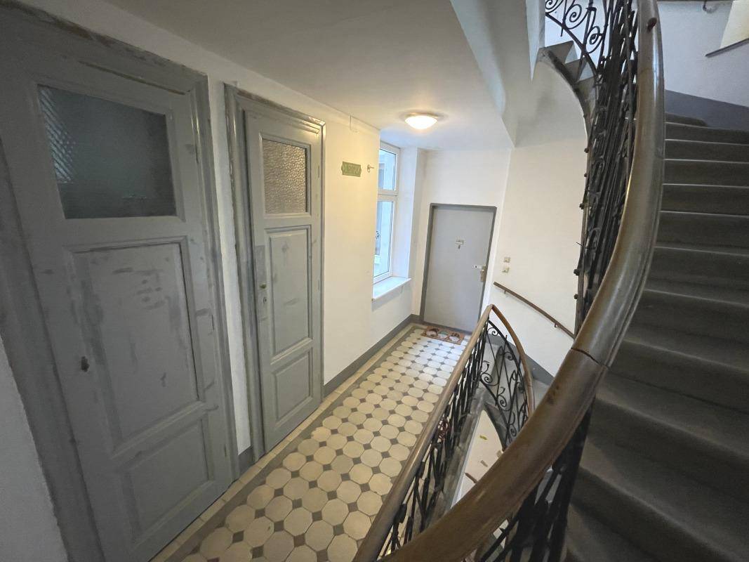Treppenabsatz in einem Altbau mit gemusterten Fliesen, mehreren Türen und einem geschwungenen Treppenaufgang.