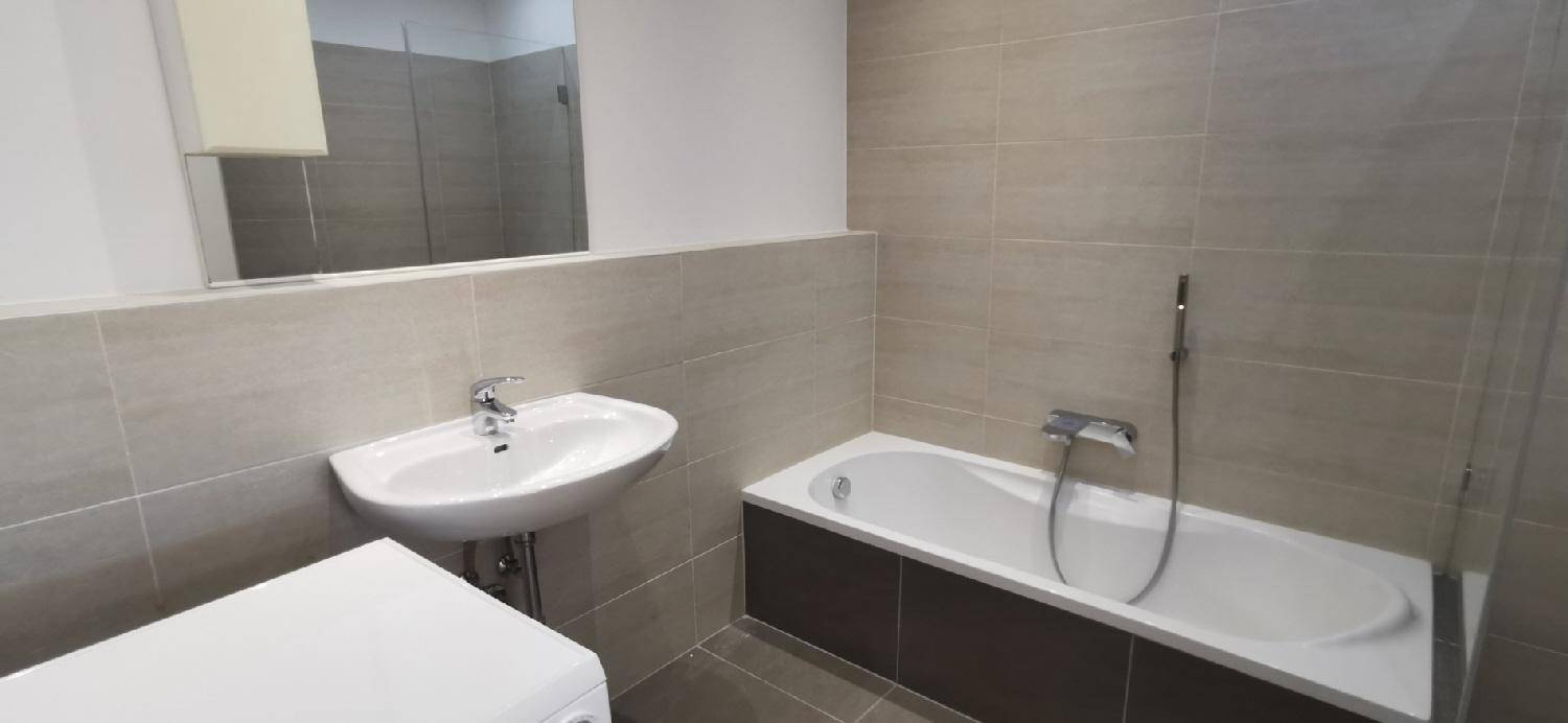 Modernes Badezimmer mit Badewanne und Waschbecken, ausgestattet mit beigefarbenen Fliesen und einem großen Spiegel.