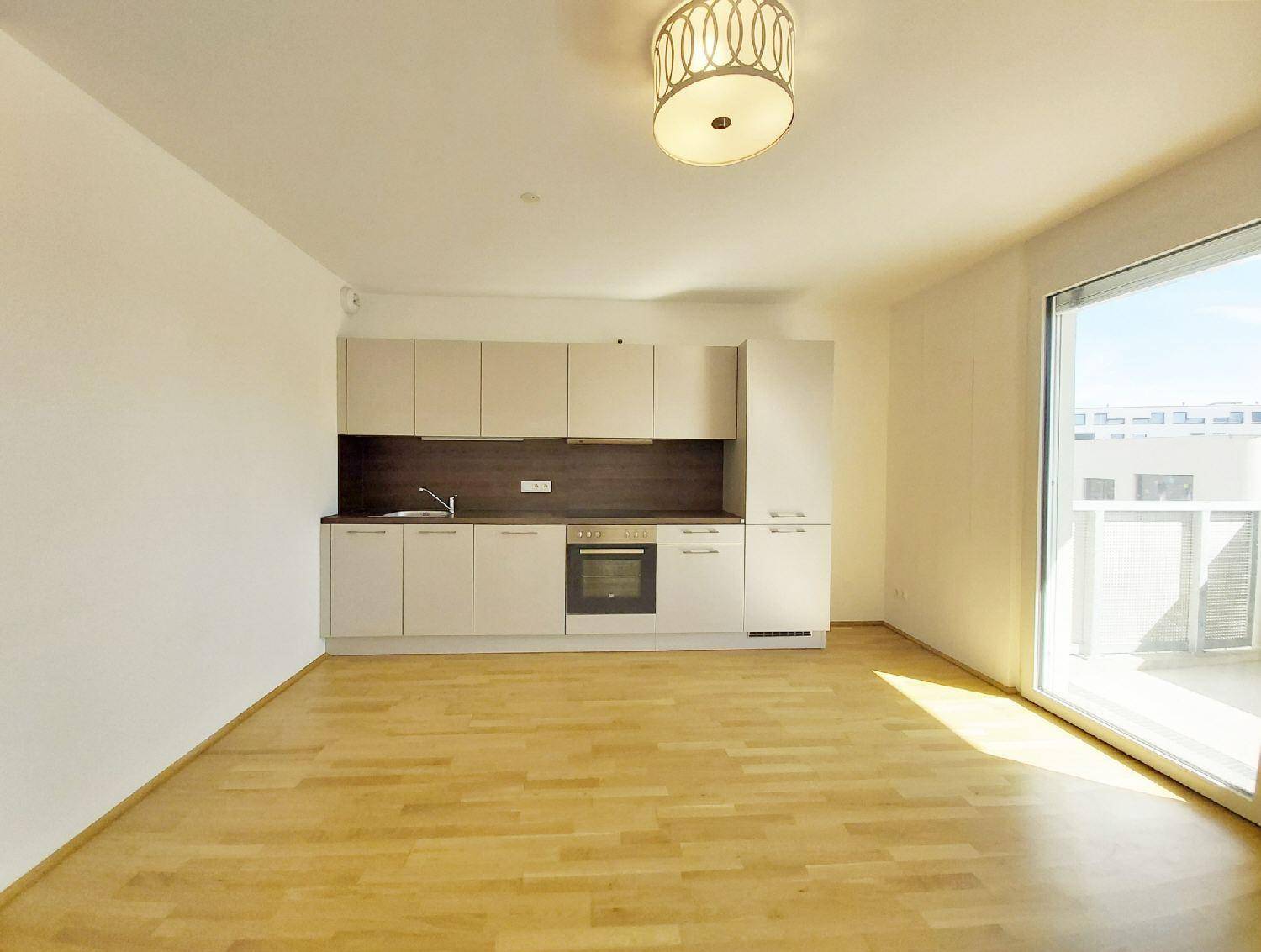 Heller offener Wohnbereich mit integrierter Küchenzeile und Zugang zu einem Balkon.